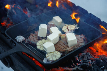 Steak on fire. Cast iron frying pan. Fresh meat. Open fire. Barbecue. Firewood.
