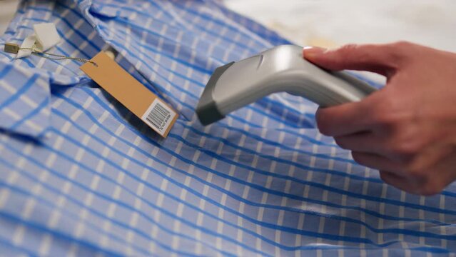 Woman at checkout scans barcode from label in clothing store. Trade, sales. Female hands scans barcode. Cashier, saleswoman scans goods. Buying shirt on coat hanger. Buying at counter. Shopping time
