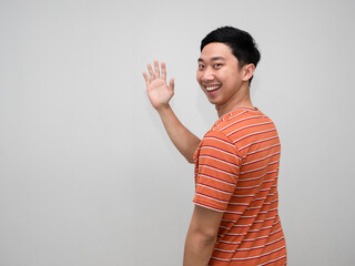 Positive man orange striped shirt cheerful smile turn around to show hand hello isolated