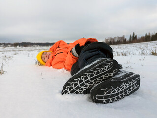 A child in winter. A boy in a bright orange jacket fell into the snow in a field in nature. The sole is a close-up.