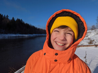 Portrait of a laughing child in a bright orange jacket against a winter landscape.