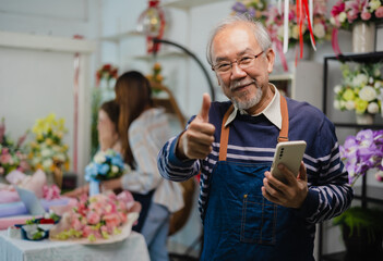 Elder senior man florist talking on smartphone using laptop at florist.portrait of mature male small business owner using laptop and looking at camera in flower shop