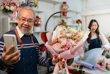 Elder senior man florist talking on smartphone using laptop at florist.portrait of mature male small business owner using laptop and looking at camera in flower shop