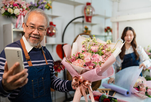 Elder senior man florist talking on smartphone using laptop at florist.portrait of mature male small business owner using laptop and looking at camera in flower shop
