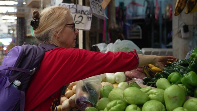 Attractive blonde mature senior woman poblano peppers, vegetables and fruit at a local indoor market in Mexico.