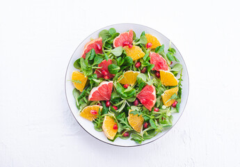 Spring salad with oranges, grapefruit, pomegranate seeds and arugula. Sweet-salty flavors. Bright, delicious recipe full of vitamins, healthy food, white background. Plant based diet