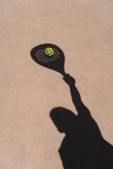 High angle of yellow ball placed on court and covered with shadow of crop person holding padel racket