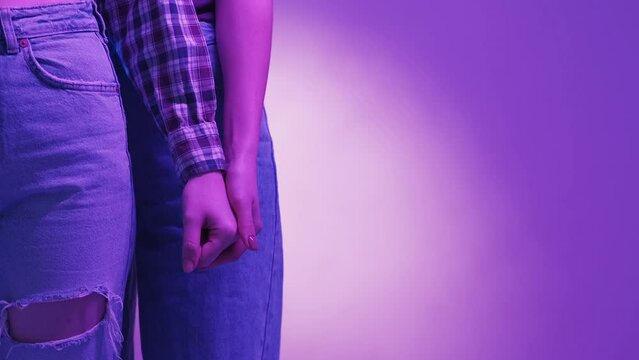 Female support. Friendly relationship. Neon light people. Unrecognizable woman holding hand of friend posing blue violet background copy space.