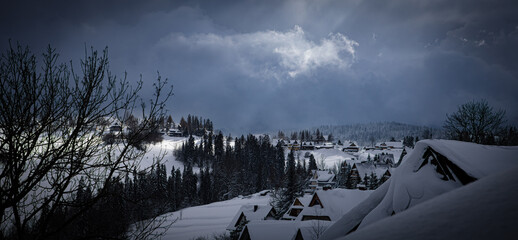 Village in the Polish mountains covered with snow, illuminated by the rays of the sun breaking through the clouds