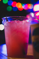 A colorful blur of lights illuminates a night scene featuring a vibrant purple drink on a table