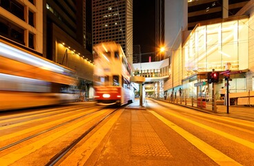 Night Scenery of downtown Hong Kong with a streetcar moving fast on the tracks among high-rise office towers ~A trolley bus traveling under a pedestrian footbridge near the Landmark Square in Hongkong