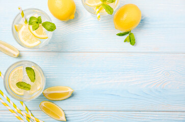 Cold refreshing summer drink with lemon and mint on light blue wooden background, top view, flat lay, copy space.
