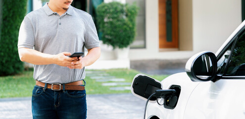 Progressive asian man install cable plug to his electric car with home charging station in the...
