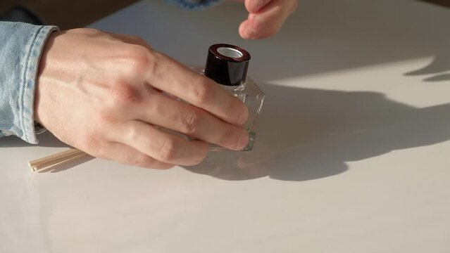 Male hanbds putting of wooden sticks into bottle of air diffuser on table