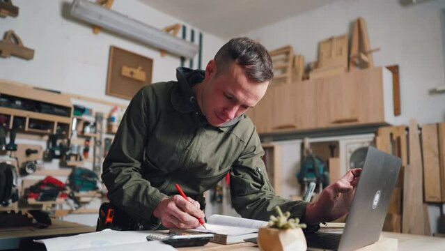 The carpenter works with documents for a new furniture order in his own workshop