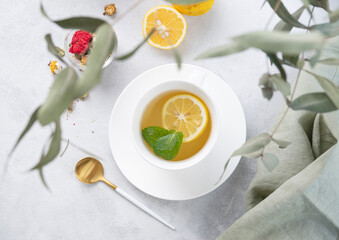 Herbal tea with lemon and mint in a white cup on a light background with eucalyptus branches. The concept of a healthy and delicious drink for immunity.