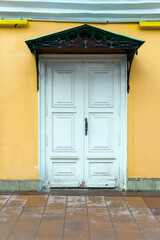 Old white wooden door with a canopy on the yellow wall