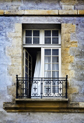 Fototapeta na wymiar Ancient building French window with white curtain, wrought iron balcony and stone walls