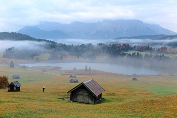 Beautiful Geroldsee on a foggy autumn morning with wooden barns on grassy fields & Karwendel...