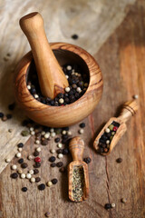 Mix of peppercorns in a wooden mortar and wooden spatulas.