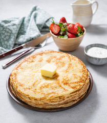 Sweet pancakes stacked with butter, sour cream and fresh strawberries on a light background.