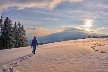 Fototapeta na wymiar nice and active senior woman snowshoeing in deep powder snow during sunset in the mountains of the Bregenz Forest Alps near Sulzberg, Vorarlberg, Austria 