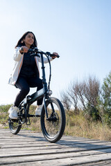 Happy latin woman riding a bike by the sea on a sunny day near to Castelldefels beach, Catalonia, Spain. 