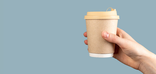 Female hand holding a paper cup of coffee over pastel blue background, banner, copy space....