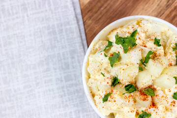 Fresh homemade traditional old-fashioned Amish Potato Salad with potatoes, boiled eggs, creamy dressing and celery in a white bowl on wooden background top view.