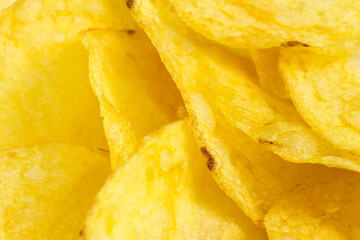 Bright yellow thin potato chips as a textured food background close up.