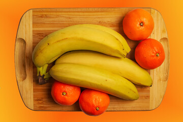 Fototapeta na wymiar A bunch of fresh ripe yellow bananas and a few orange tangerines on a wooden kitchen board.