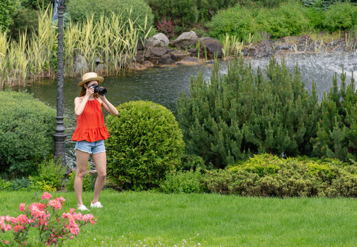 portrait of a beautiful hipster girl with a camera taking photos and stand on a lake slide in the park