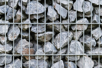 Raw rocks border and gray stones wall as natural stones background with crushed and rough material stacked in metal grid as massive border in gray colors as natural mineral background for gardens