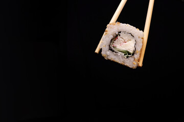 Chopsticks hold sushi on black background. copy space for text