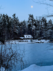 Winter landscape of a snowy pine forest, a wooden house and a frozen lake