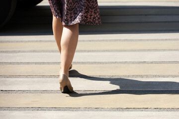 Woman in short dress and pumps shoes crossing the road by crosswalk on car background car. Female legs on city street