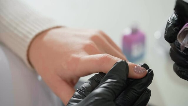 Nail service. Woman getting nails done at beauty salon. Manicure master applying nails polish for woman client. Close-up