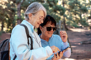Caucasian senior couple of females friends looking at smartphone while hiking in the woods. Elderly people checking the right direction on the online map enjoying healthy lifestyle in mountain