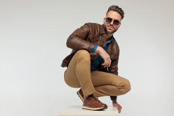 casual man resting arms, squatting and looking at the camera
