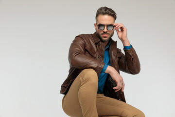 casual man resting arms, squatting and fixing sunglasses