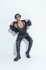 curly young arab man with sunglasses adjusting and pulling leather jacket
