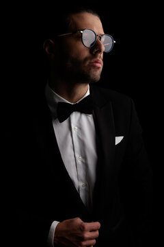 handsome elegant man with glasses looking to side while fixing tuxedo