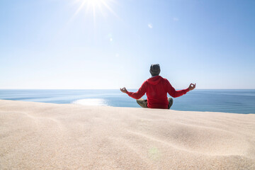 Mature man, over fifty years old. Meditating on the sand dunes. The dunes, the sea, the blue sky and the sun as a background.