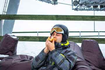 a snack at the ski resort. the guy eats on the ski slope
