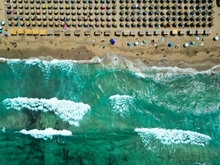 Vertical aerial view of long sandy beach with big white waves and umbrellas