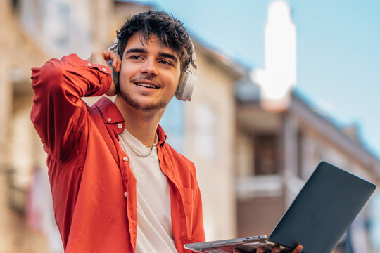 young man with headphones and laptop listening to music outdoors