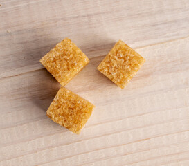 Three brown sugar cubes, close-up, on a white wooden table, top view.