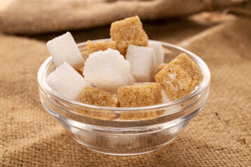Several cubes of brown and white sugar, close-up, on a jute fabric.