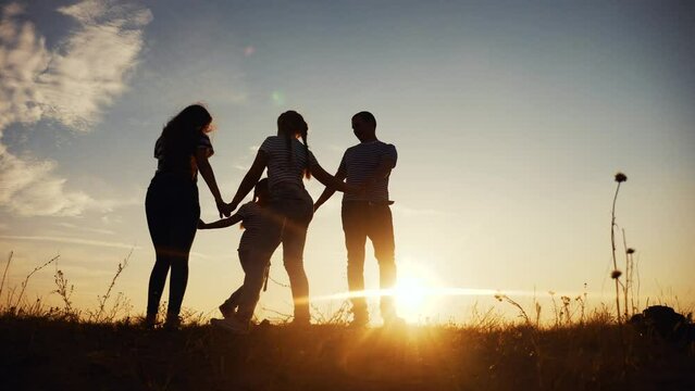 happy family mom dad and daughter play round dance silhouette at sunset. people in park kid dream concept. happy fun family parents with little kid child daughter play in park on grass holding hands