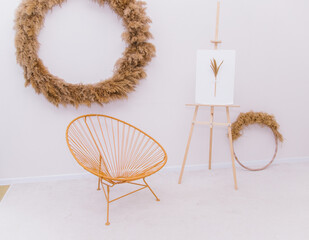 A wicker round chair stands against the wall. Bright and spacious room.Wicker chair, handmade. On the wall is a decoration made of dry reeds and grass.